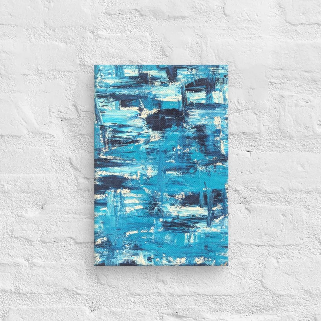 Canvas print of the abstract painting "Blue Streak" with layered blue and white brushstrokes, displayed on a white brick wall in a minimalist interior setting.