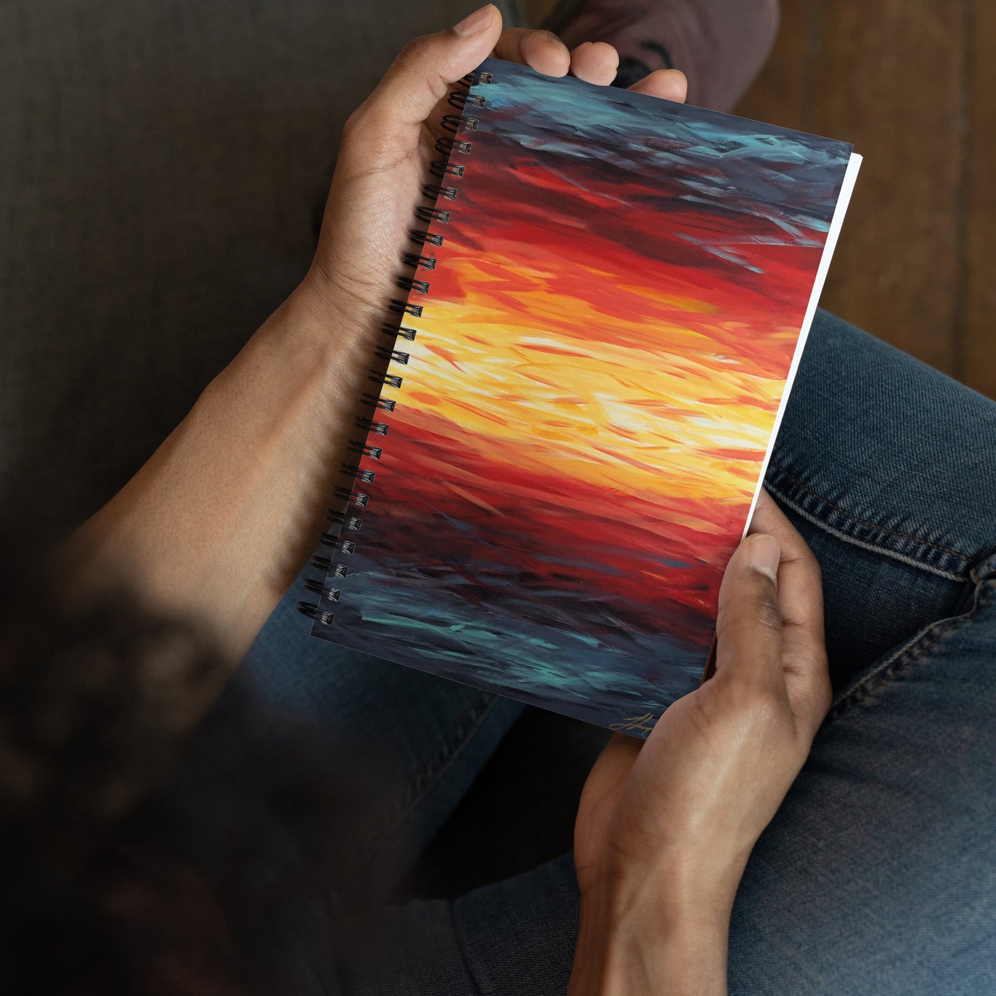 Abstract painting of a sunset with blue, red, yellow, and white on a spiral notebook in a persons hands