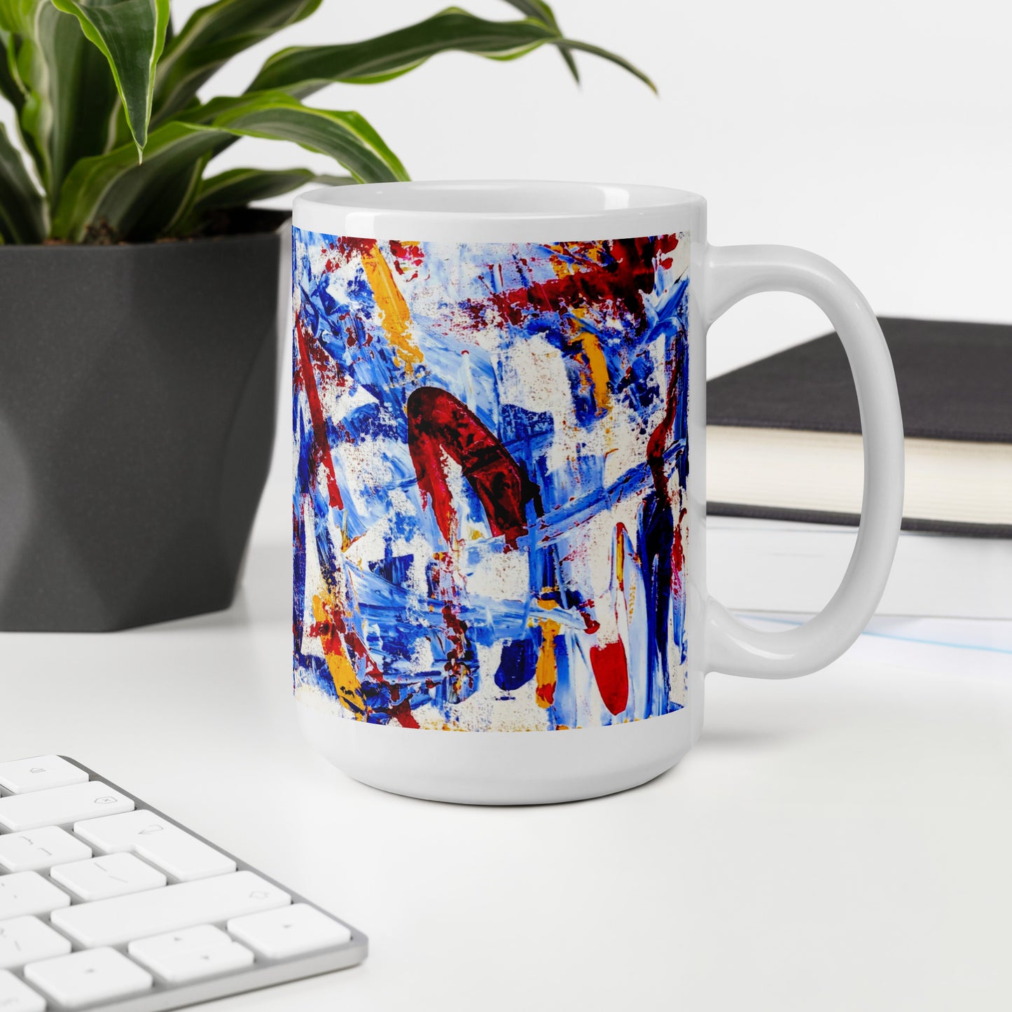 Ceramic mug featuring the abstract artwork "Rebel Parade" with bold red, blue, and white brushstrokes wrapping around the surface, shown in an office setting.