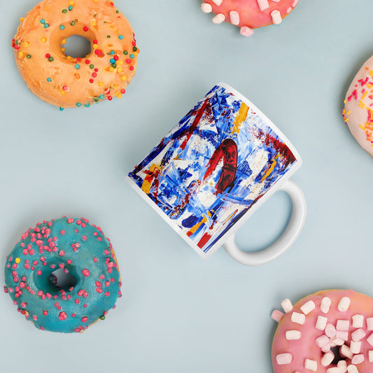 Ceramic mug featuring the abstract artwork "Rebel Parade" with bold red, blue, and white brushstrokes wrapping around the surface, shown with colorful donuts.